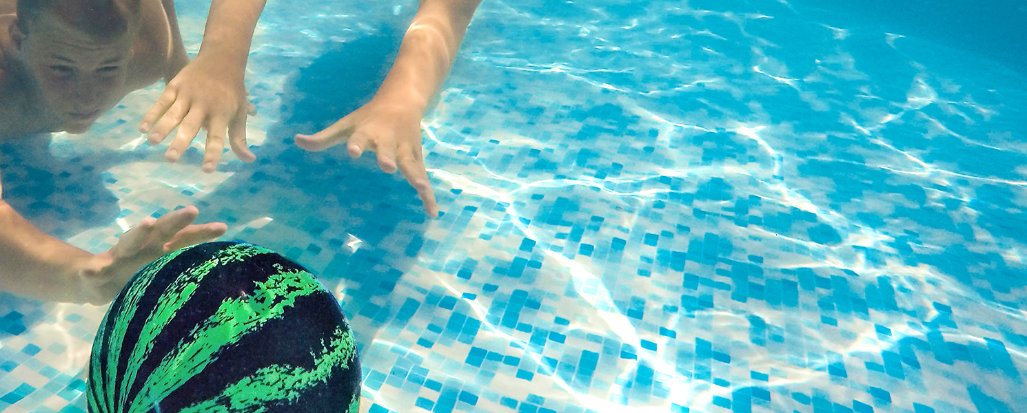 Two swimmers passing a watermelon ball along the floor of a pool